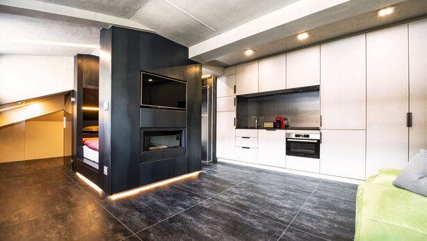 A modern kitchen with dark tiles, built-in appliances, and a green sofa. - Loft on 1236 129A (Ortisei)