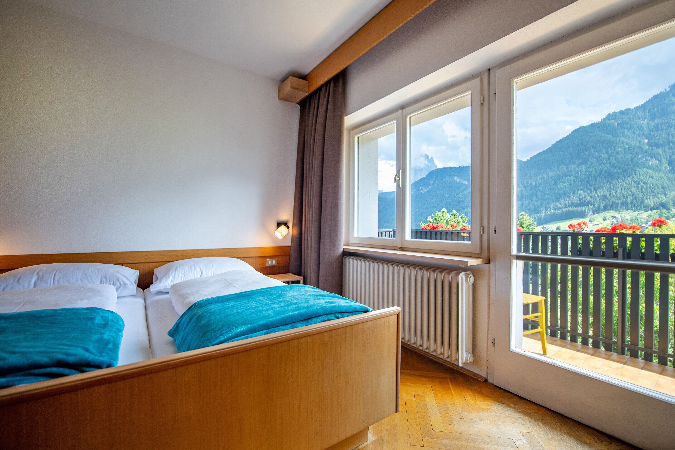 A bedroom with a wooden bed, a view of mountains, and a balcony with a chair.