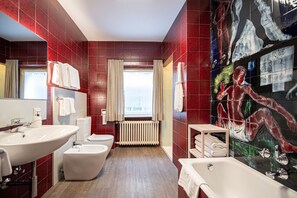 A bathroom with red tiled walls, a large mirror, a bathtub, a toilet, and a bidet.
