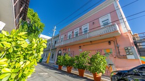 Un bâtiment rose doté d’un balcon, de plantes en pot et donnant sur la rue.