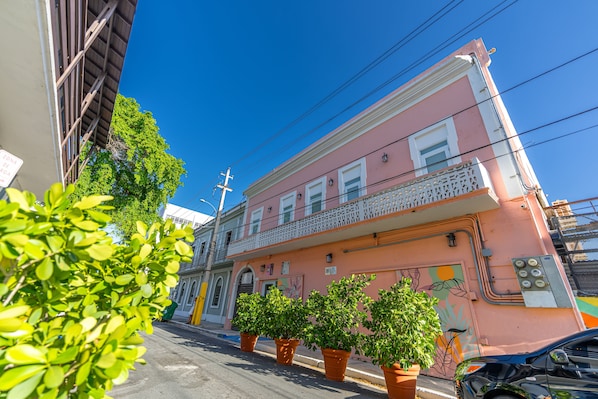 A pink building with a balcony, potted plants, and a street view.