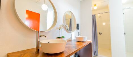 Une salle de bain avec un meuble-lavabo en bois, deux miroirs ronds, un lavabo blanc et un espace douche.