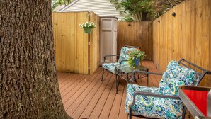 A wooden deck with a metal table and two patterned chairs, a hanging flower pot, and a wooden fence. - Rehoboth Beach Efficiency Downtown Deck Sleeps 2 (Rehoboth Beach)
