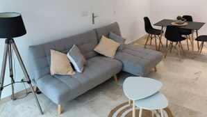 En moderne stue med en grå hjørnesofa, et lille hvidt bord og et spiseområde med et sort bord og stole.