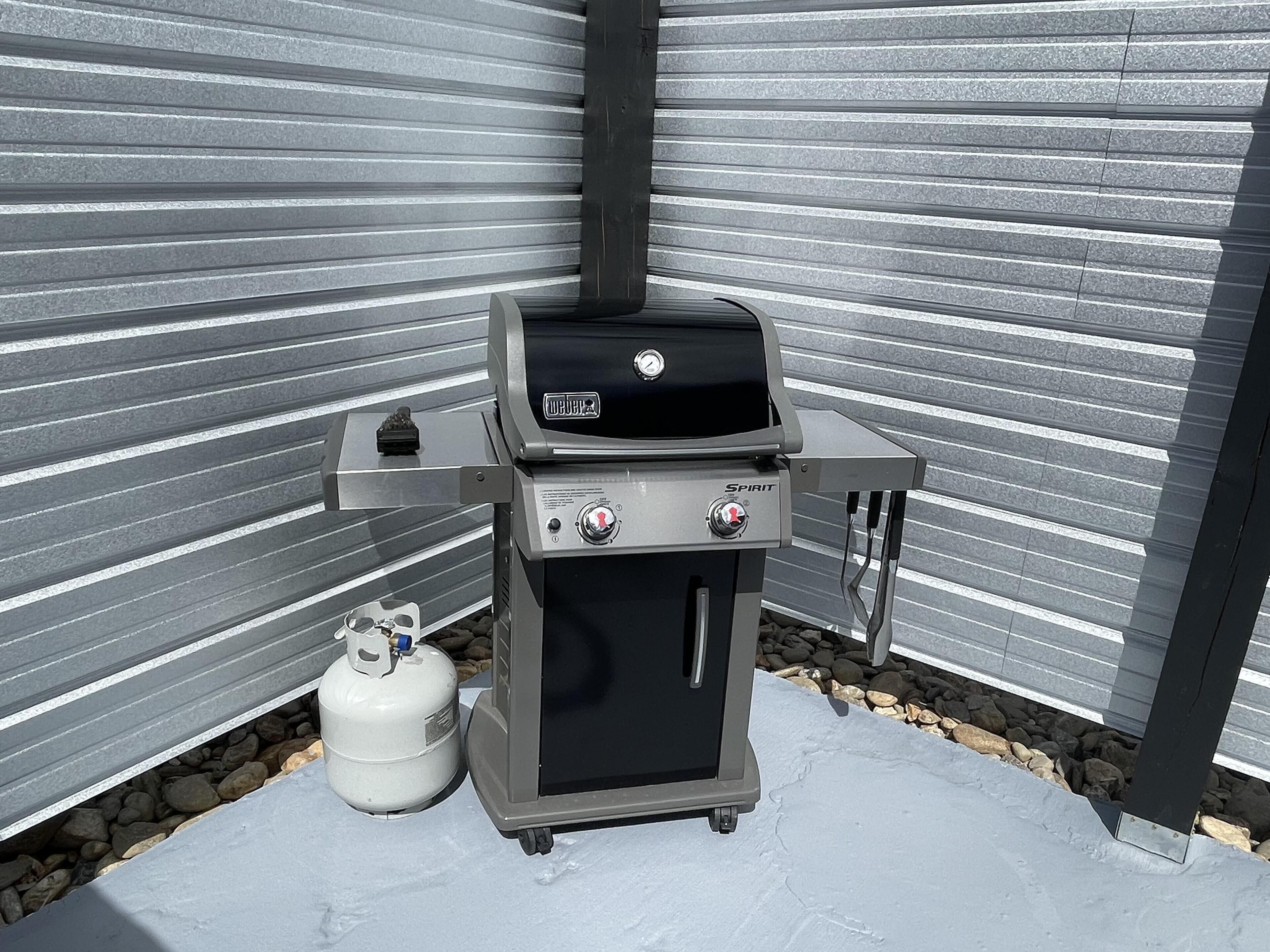 Un barbecue au gaz portatif doté d’un écran numérique et de boutons de commande, placé sur une surface en béton, avec une bouteille de gaz à proximité.