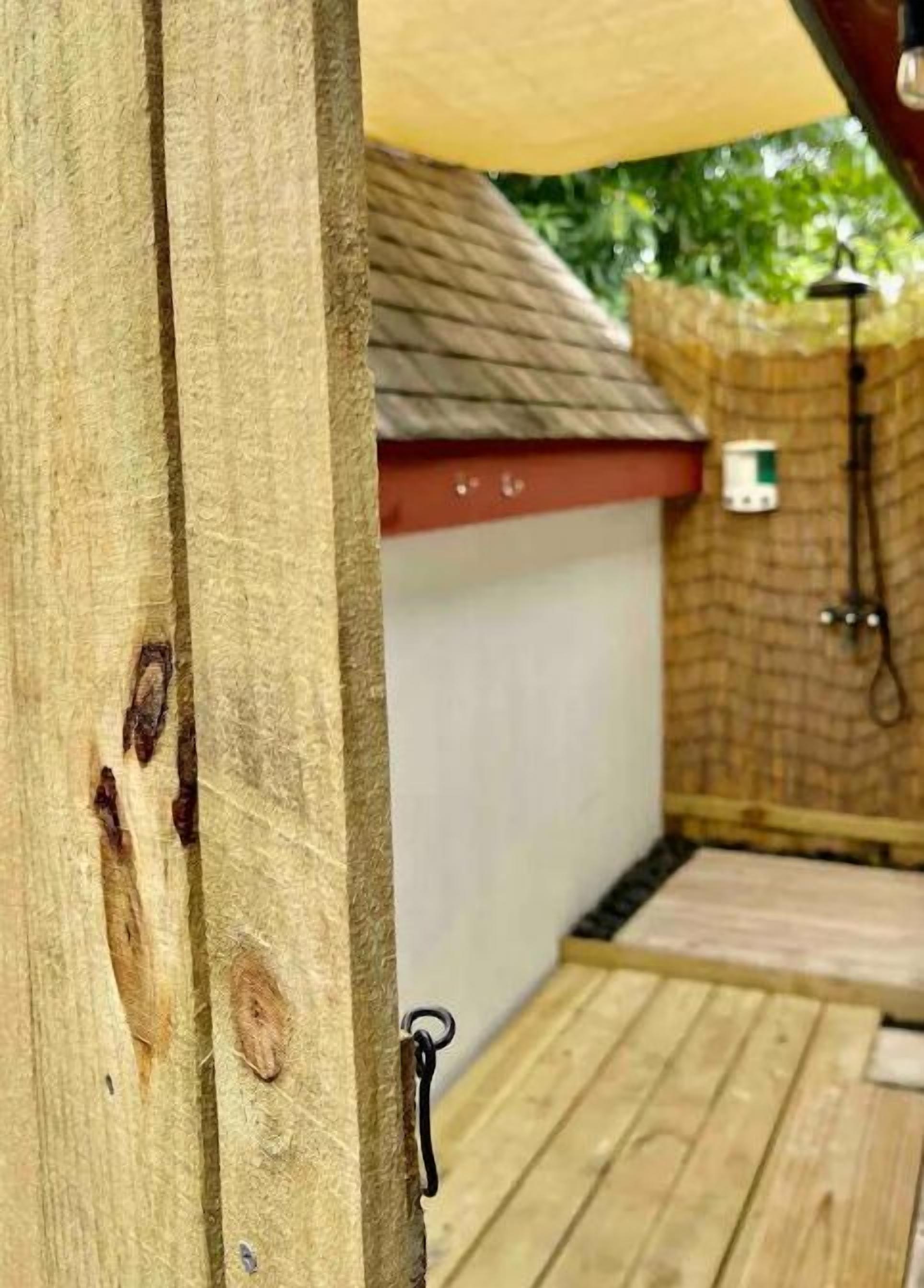 Eine Holzterrasse mit Metallgeländer, ein kleines Gartenhaus mit rotem Dach und eine Backsteinmauer mit einem Schlauch im Hintergrund.