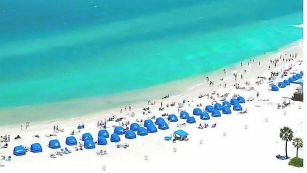 A beach with white sand and clear turquoise water. There are blue umbrellas and people on the beach. - Boho Bungalow! Guesthouse near Downtown & Beaches!  (St. Petersburg)