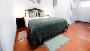 A bedroom with a bed, nightstands, a green blanket, and a green wall decoration.