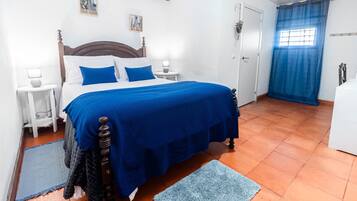 A bedroom with a bed, two bedside tables, a nightstand, a window with blue curtains, and a door.