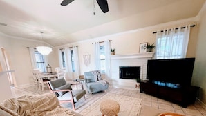 A living room with a sofa, chairs, a TV, a fireplace, and a dining area with a table and chairs. - Padre Island house with private pool (Corpus Christi)
