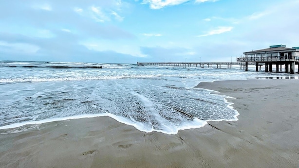 A beach with a pier extending into the ocean, a building on the pier, and waves approaching the shore. - Padre Island house with private pool (Corpus Christi)