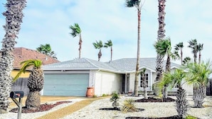 A residential area with multiple palm trees, a house with a grey garage, and a clear sky. - Padre Island house with private pool (Corpus Christi)