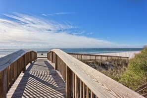 A wooden boardwalk leading to a beach with a clear view of the ocean and sky.