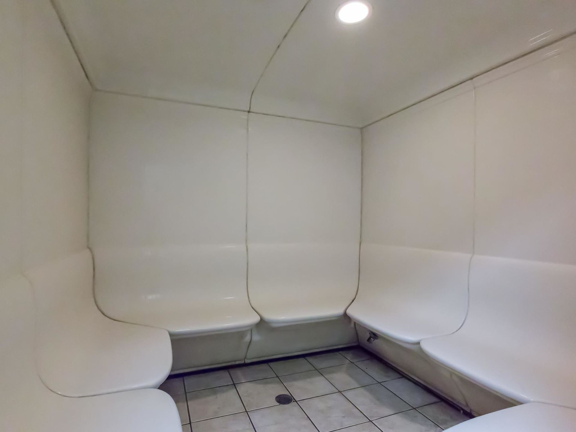 A small, tiled bathroom with three white toilets and a single light fixture on the ceiling.