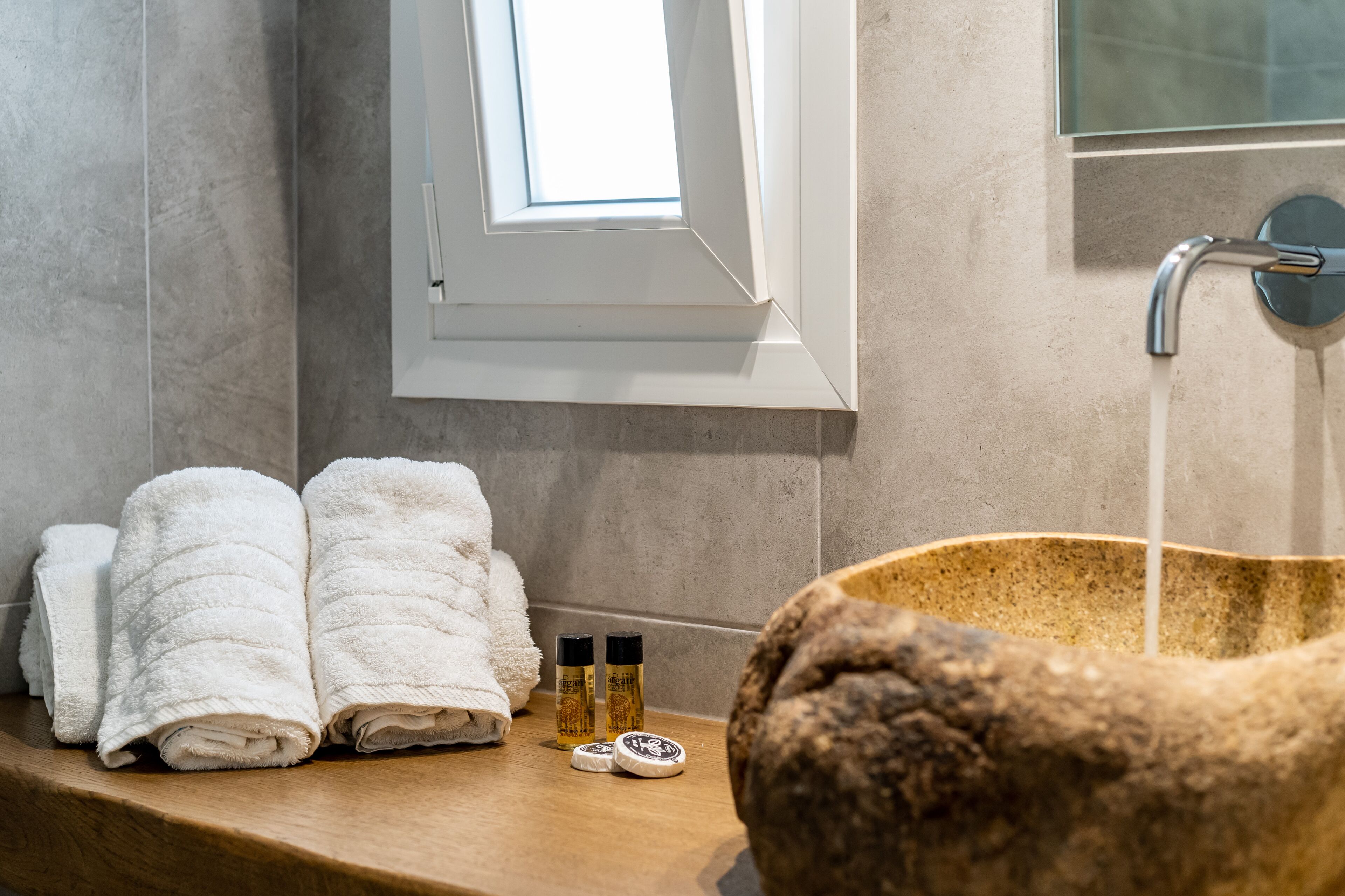 A bathroom with a wooden vanity, a white towel, two bottles of soap, and a stone basin.