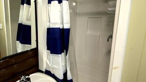 Un baño con lavamanos blanco, un espejo y zona de ducha con cortina a rayas azules y blancas.