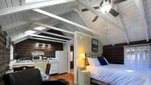 Una habitación de estilo cabaña de madera con cama, escritorio, silla y kitchenette.