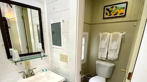Un baño con un lavamanos blanco, muebles oscuros, un espejo y una zona de ducha.