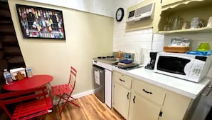 Una cocina compacta con una mesa y sillas rojas, un microondas y una cafetera.