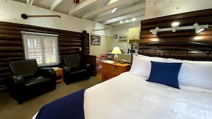 Una habitación de hotel con una cama grande, dos sillas, un escritorio y un ventilador de techo.