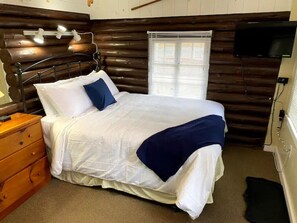 Cozy bedroom with a made bed, nightstand, dresser, and TV.