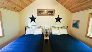 Una habitación con dos camas, un ventilador de techo, un cuadro enmarcado y dos estrellas en la pared.