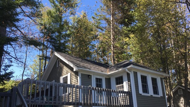 A two-story cabin with a balcony, surrounded by trees.