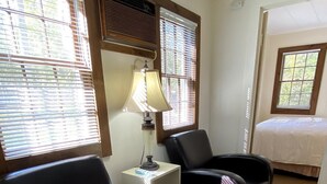 A hotel room with two black leather chairs, a small bedside table with a lamp, and a bed with a white cover.