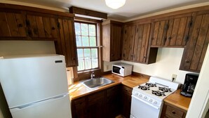 A compact kitchen with wooden cabinets, a refrigerator, a microwave, a stove, and a sink.