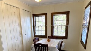 A dining room with a table set for four, two windows with blinds, a ceiling light, and a white door.