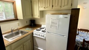Una cocina compacta con armarios blancos, estufa, refrigerador y ventana con persianas.
