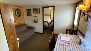 A hotel room with a wooden wall, a sofa, a dining table with chairs, and a bed with a headboard.