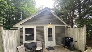 A small wooden deck with a table and chairs, a barbecue grill, and a shed with a door and windows.