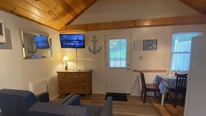 A cozy room with a wooden ceiling, a TV mounted on the wall, a door with a window, and a small table with chairs.