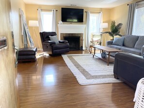 Relax in the comfortable seating area with a black leather recliner and a sofa, featuring a flat-screen TV above a fireplace.