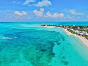 Vista aérea de un complejo turístico costero con playa de arena, aguas turquesas cristalinas y un pequeño bote a lo lejos.