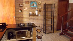 A kitchen with a brick wall, a microwave, a coffee station, and a wooden staircase.