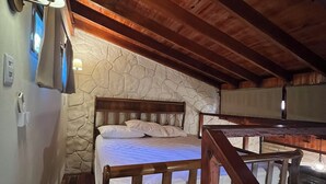 A wooden ceiling, a stone wall, a bed with white bedding, a nightstand, and a lamp.