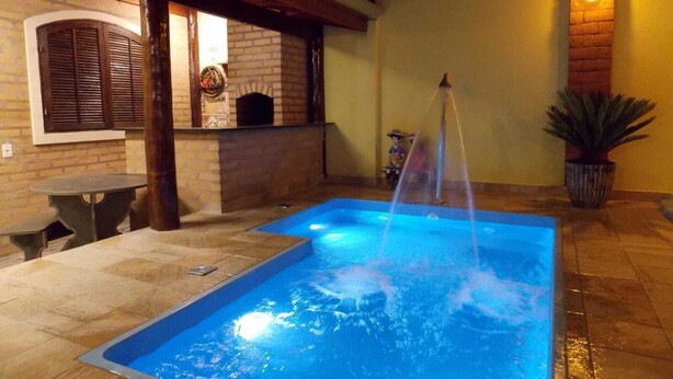 A swimming pool with a fountain, a brick fireplace, and a table and chair set up for outdoor dining.
