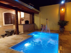Una piscina con una fuente, una chimenea de ladrillo y un conjunto de mesa y sillas para comer al aire libre.