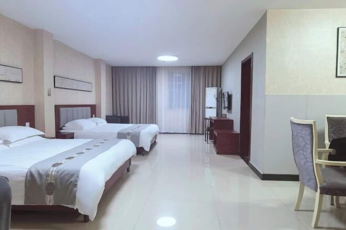 A hotel room with two beds, a desk, a chair, a television, and a window with curtains.