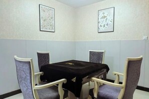 A dining area with a table and four chairs, two framed artworks on the walls, and a white wall with a black baseboard. - Wanding Business Hostel (Xinchang)