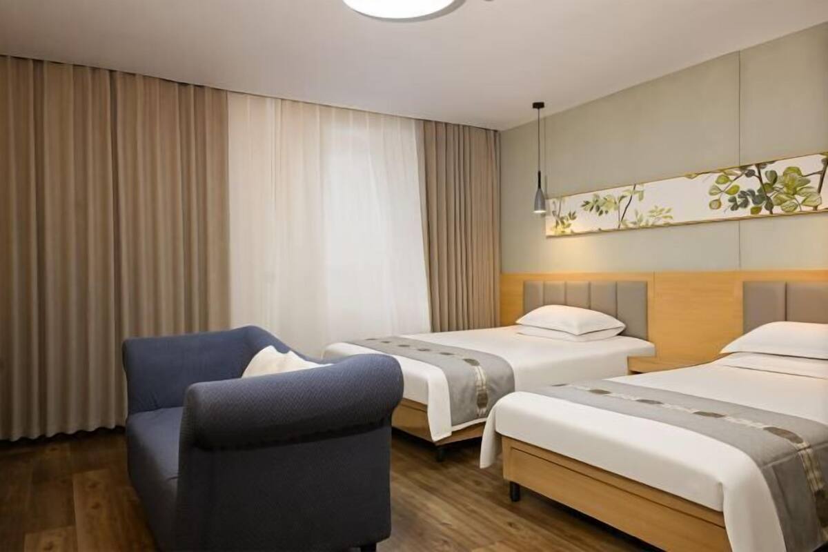 A hotel room with two beds, a blue armchair, and a decorative wall panel.