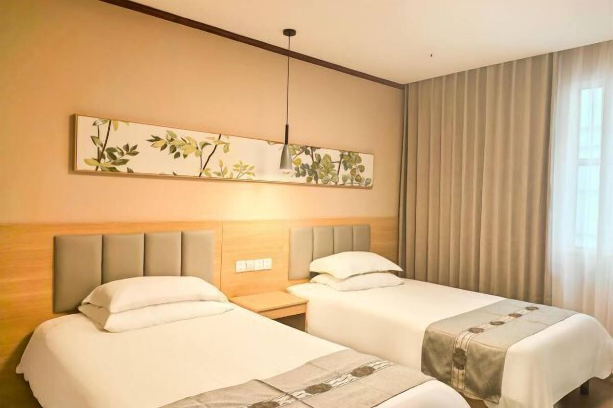 A hotel room with two beds, a headboard, a nightstand, a wall-mounted artwork, and a window with curtains.