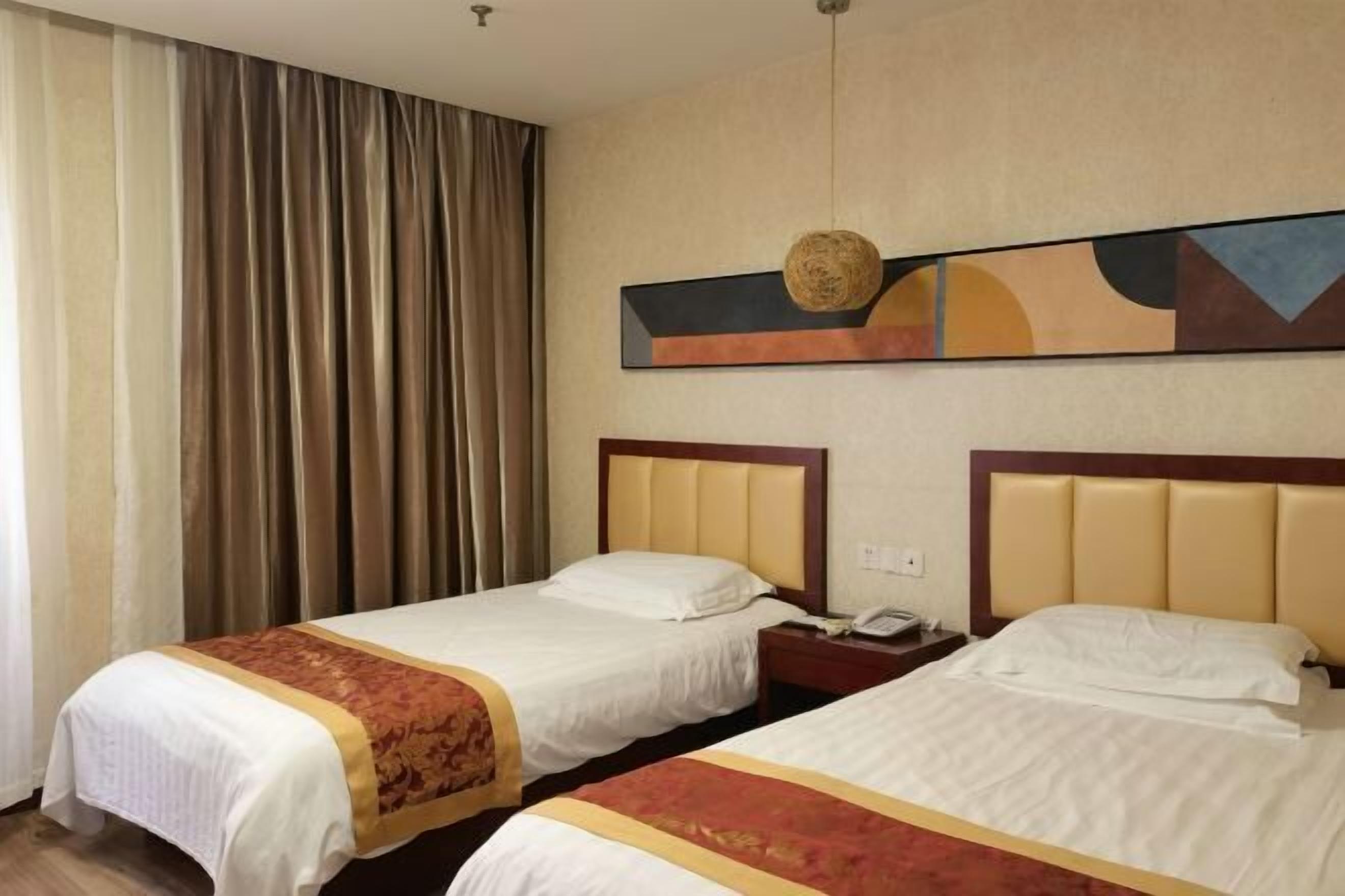 A hotel room with two beds, a large window with curtains, a wall-mounted artwork, and a telephone on the nightstand.