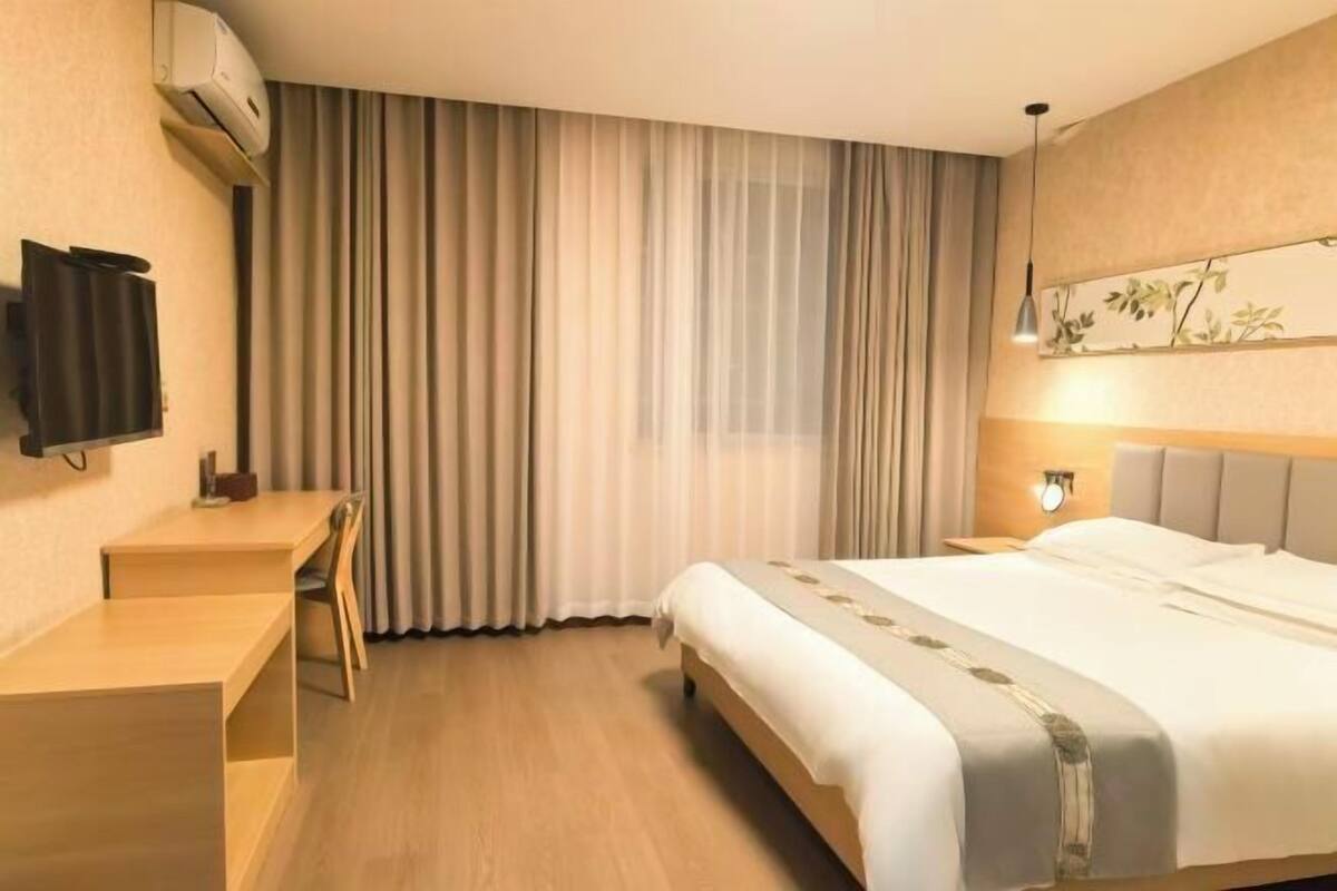 A hotel room with a bed, a desk, a chair, a TV, and a window with curtains.