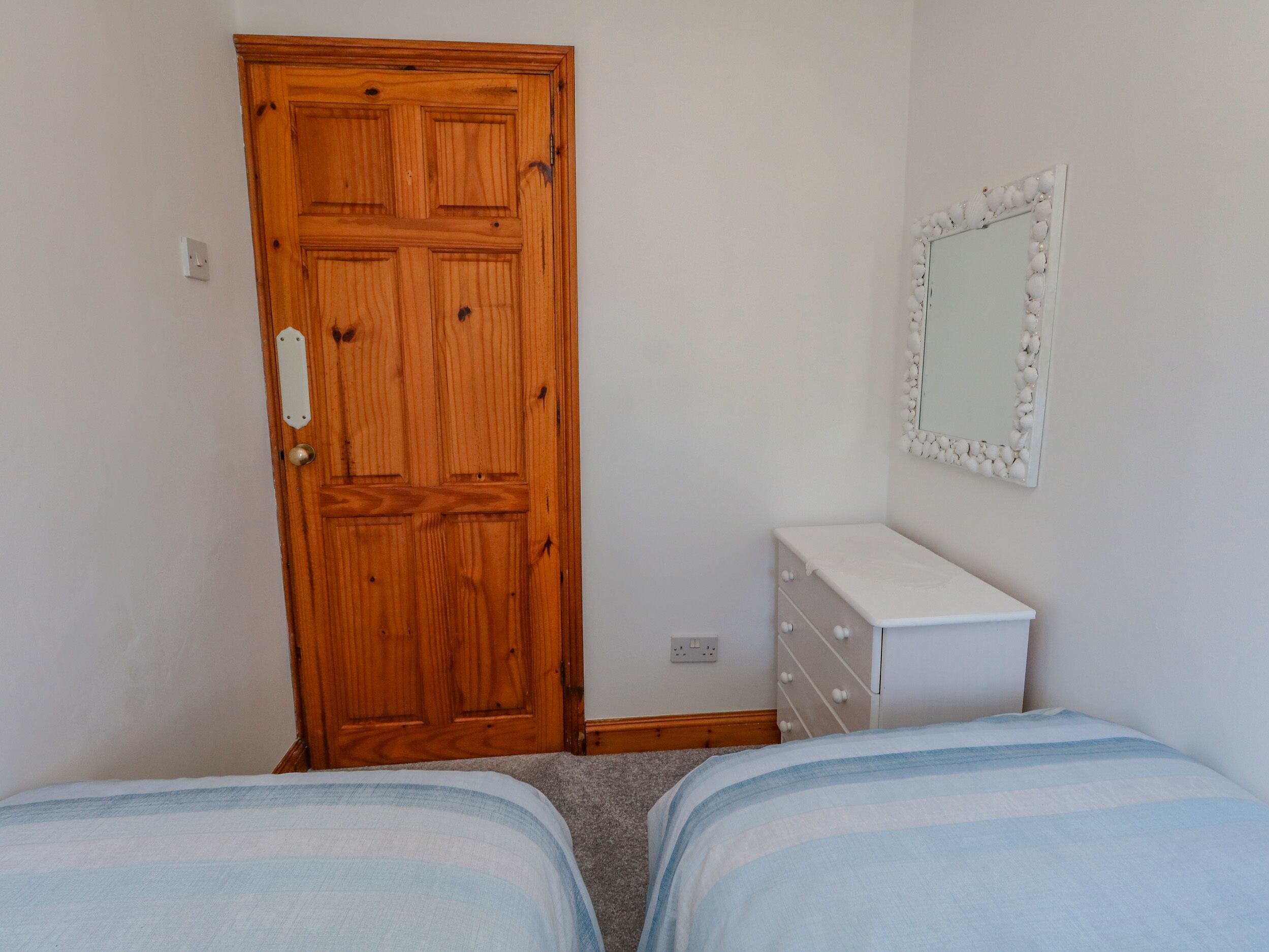 A bedroom with two beds, a wooden door, a dresser, and a mirror on the wall.