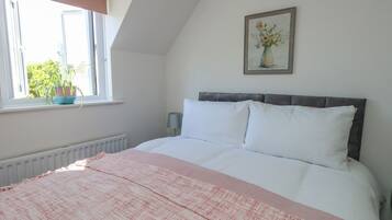 Ett sovrum med en säng, ett fönster med utsikt, ett element och en tavla på väggen.