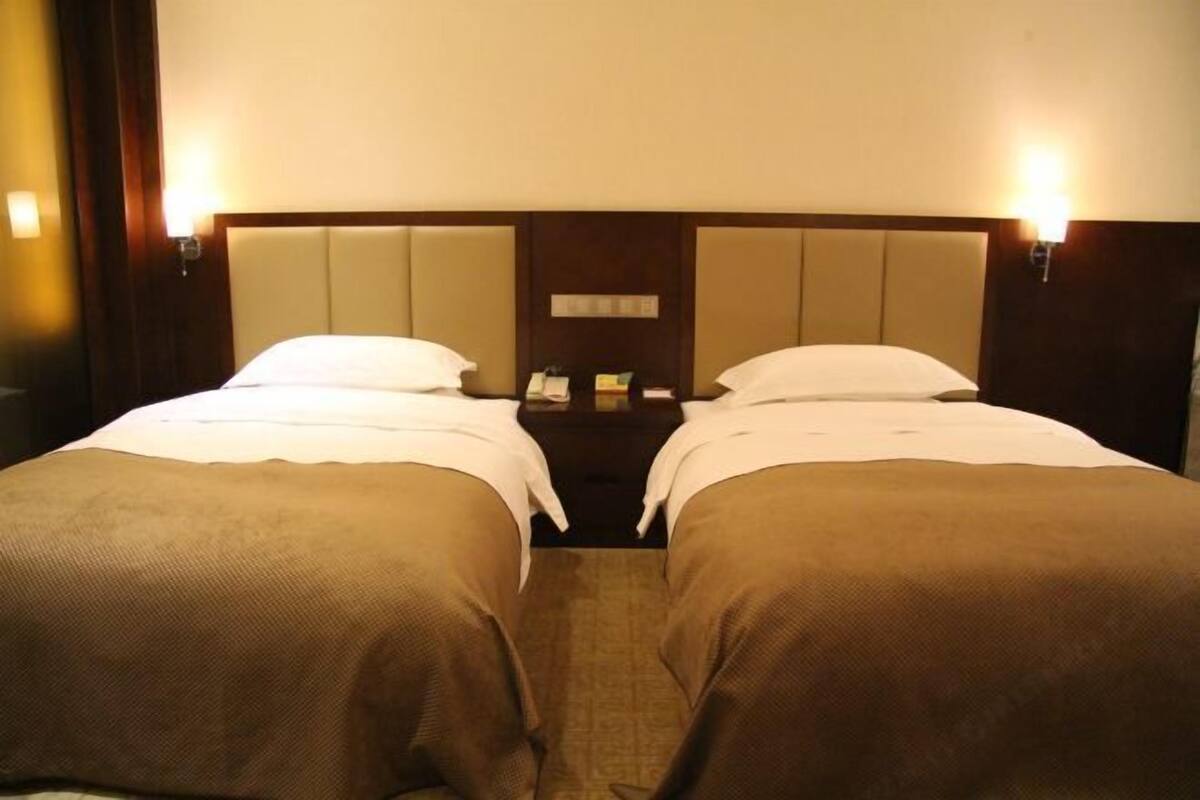 Een hotelkamer met twee enkele bedden, een hoofdbord met een spiegel, bedlampjes en een nachtkastje met een telefoon.