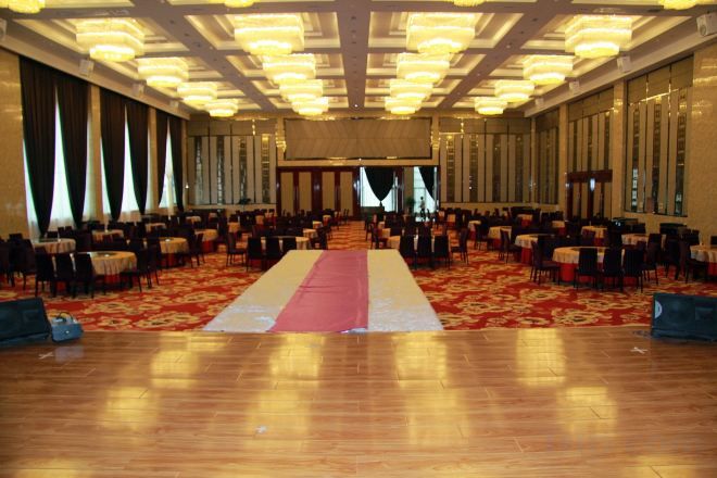 A large hall with rows of tables and chairs, a central aisle, and a carpeted floor.